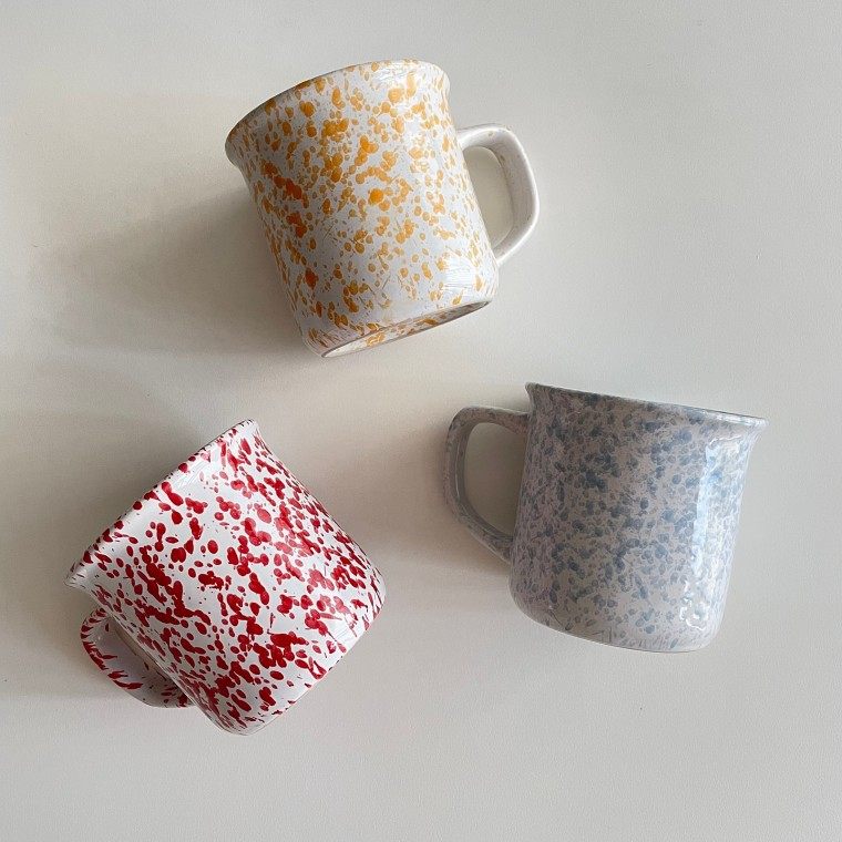 Three splatter-glaze ceramic mugs in yellow, red and blue